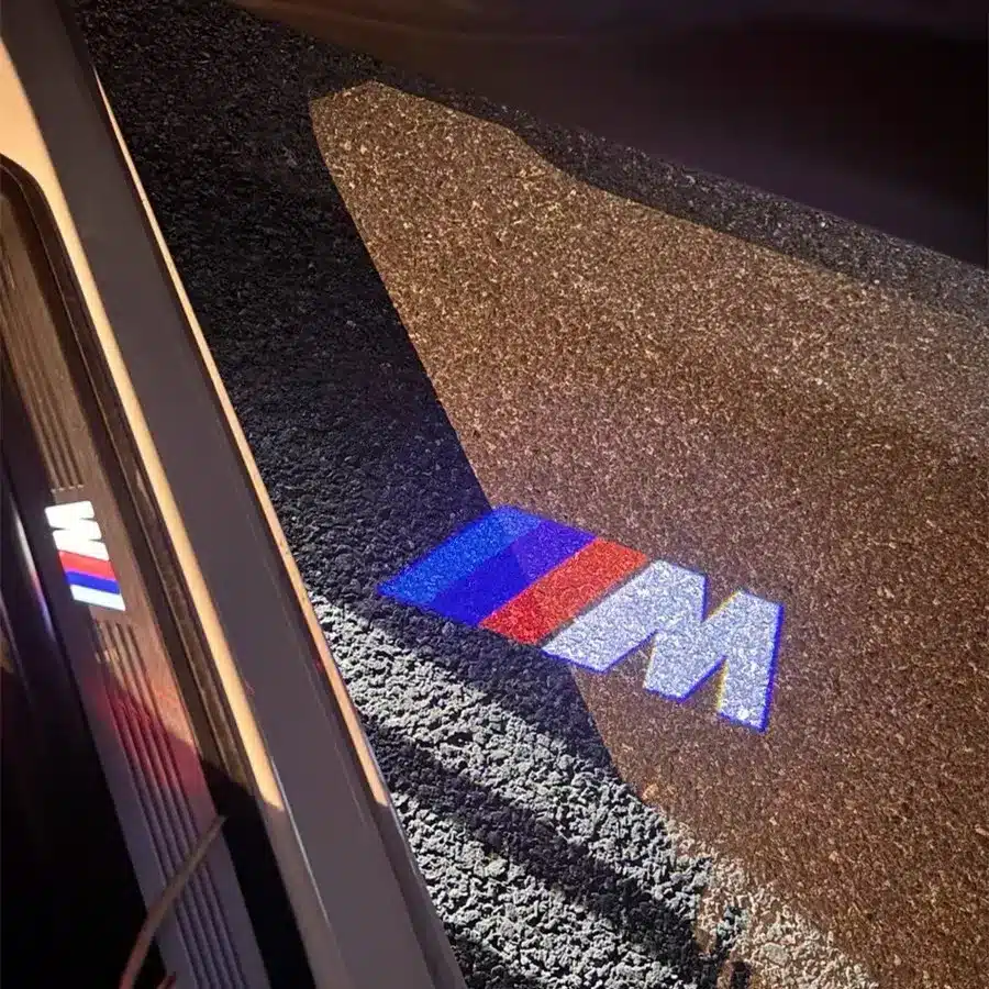 BMW M Door Lights| LED BMW M Door Lights A car door projects the BMW M logo in blue, purple, and red onto the ground next to the vehicle.