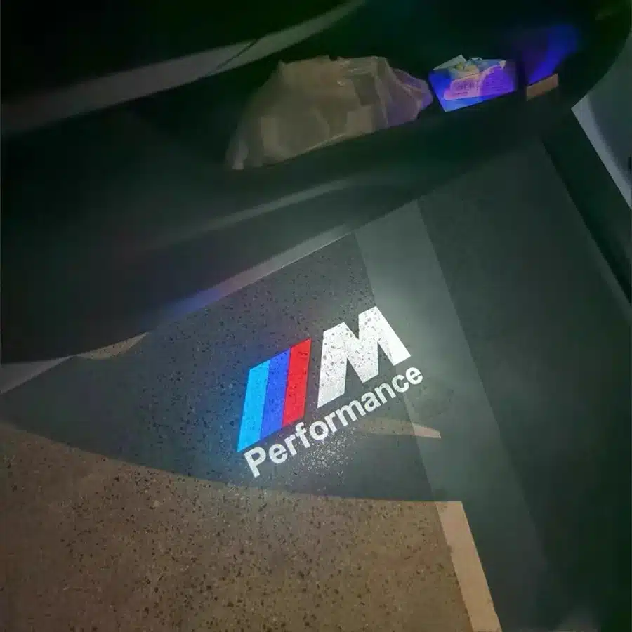 BMW M Sport Door Lights| BMW M Sport Door Lights Logo Projector Car door opens to reveal illuminated "M Performance" logo in blue, purple, and red projected on the ground, suggesting luxury and sporty design.